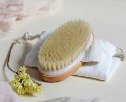 Cepillo con mango de madera sobre bolsa blanca, junto a flores amarillas.