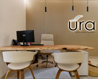 Oficina moderna con escritorio de madera y logo de "Ura Hotels and Resorts".
