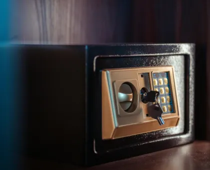 Caja fuerte negra con panel num&eacute;rico y llave incrustada, sobre estante de madera.