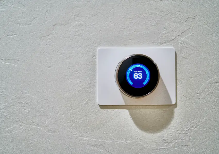 Termostato inteligente en pared con pantalla azul mostrando 63 grados.