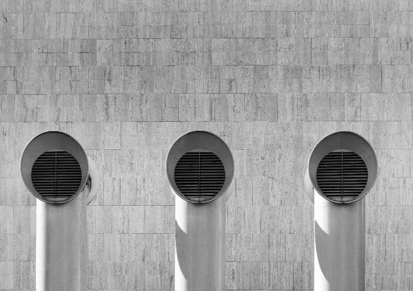 Tres tubos redondos en una pared de piedra con rejillas met&aacute;licas.