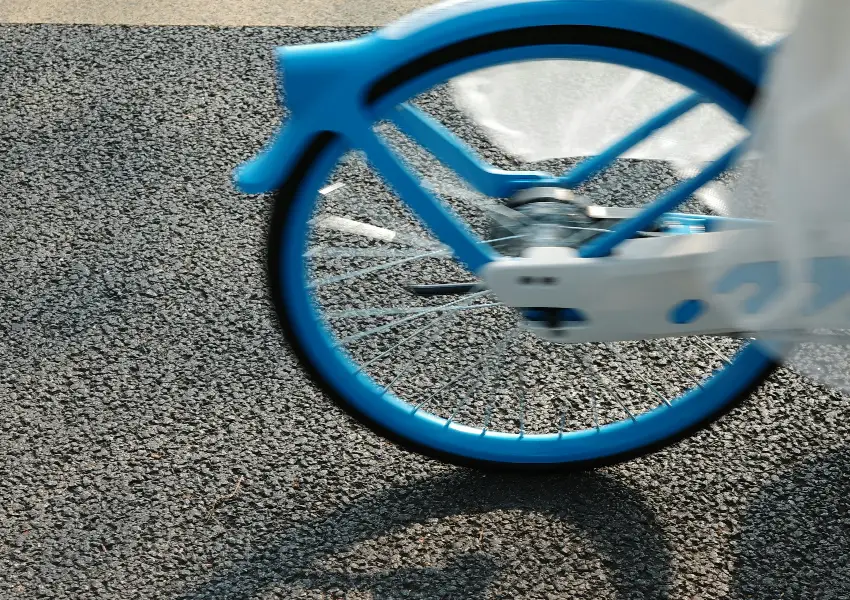 Rueda trasera de bicicleta azul girando en carretera asfaltada.