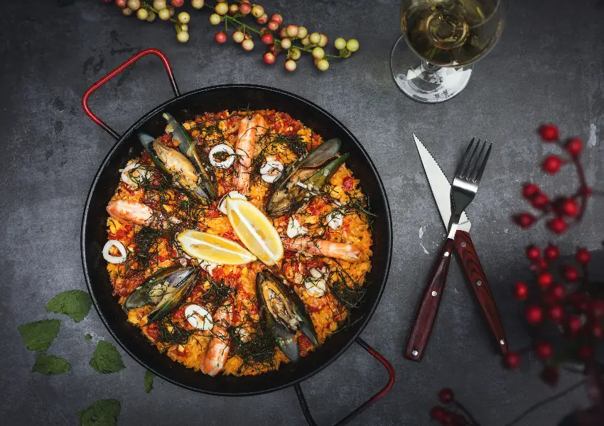 Paella de mariscos en sart&eacute;n negra con rodajas de lim&oacute;n y copa de vino.