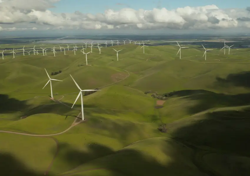 Campos verdes con m&uacute;ltiples aerogeneradores bajo un cielo nublado.