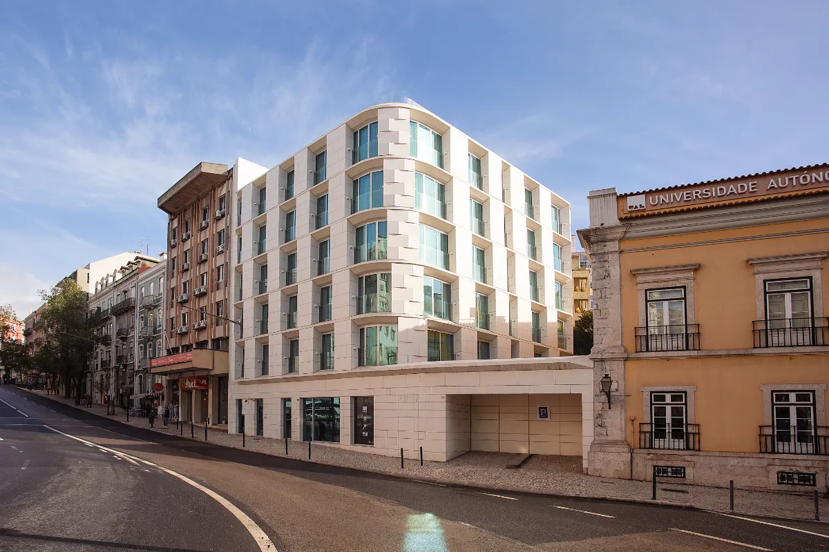 Edificio moderno junto a una universidad y una calle vacía bajo un cielo despejado.