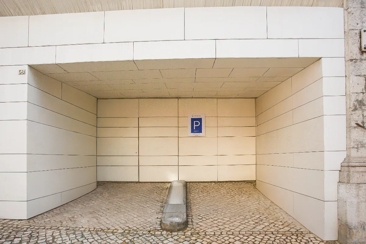 Espacio de estacionamiento vacío con un cartel de "P" en la pared blanca y suelo de adoquines.