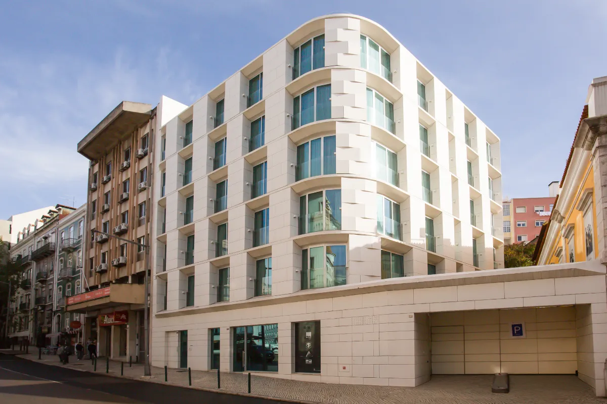Edificio moderno de seis pisos con fachada blanca y ventanas grandes en una calle urbana.