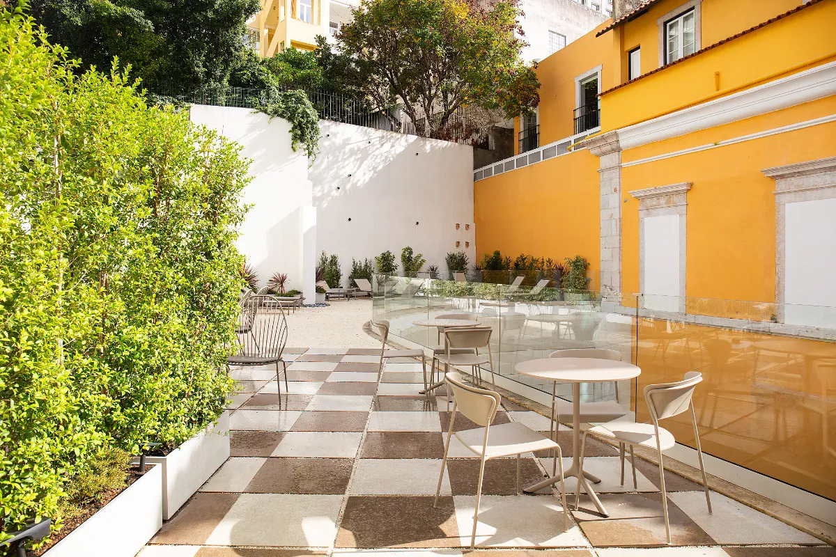 Patio con sillas, mesas, plantas y paredes de color amarillo y blanco.