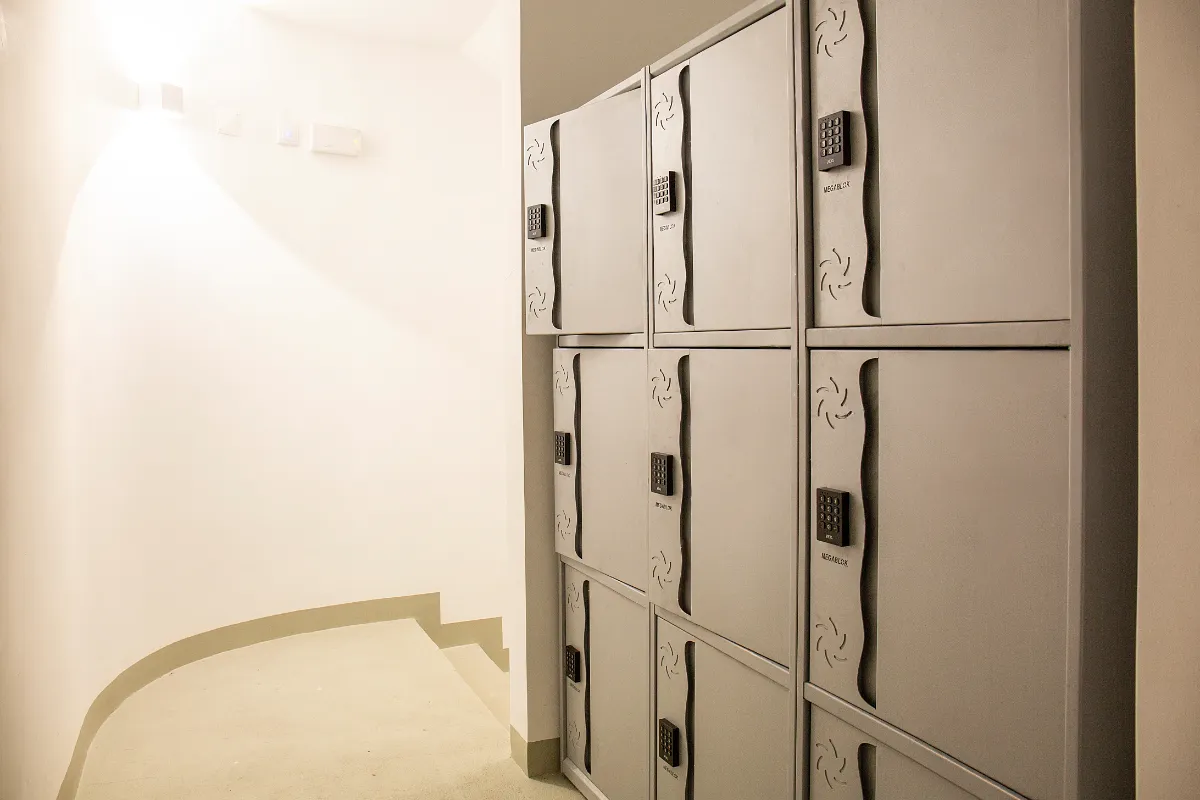 Pasillo iluminado con casilleros grises a la derecha equipados con cerraduras electrónicas.