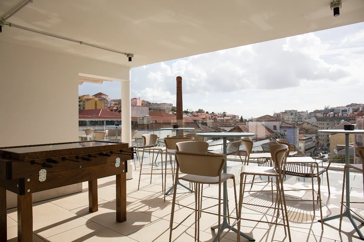 Terraza con futbolín y sillas altas, ofrece vista urbana de una ciudad con cielo parcialmente nublado.