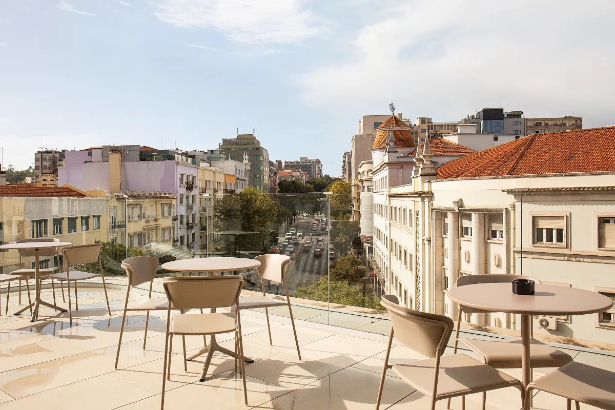 Terraza con mesas y sillas, vista a la ciudad con edificios y calles arboladas.
