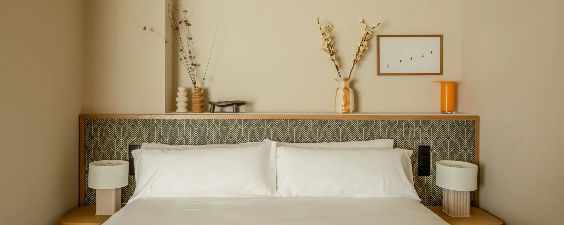 Cama minimalista con decoraci&oacute;n sencilla y l&aacute;mparas de mesa blancas.