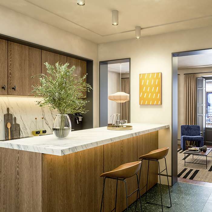 Cocina moderna con isla de m&aacute;rmol, sillas altas y decoraci&oacute;n minimalista.