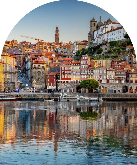 Cidade do Porto &agrave; beira do rio ao entardecer, com reflexos coloridos na &aacute;gua.