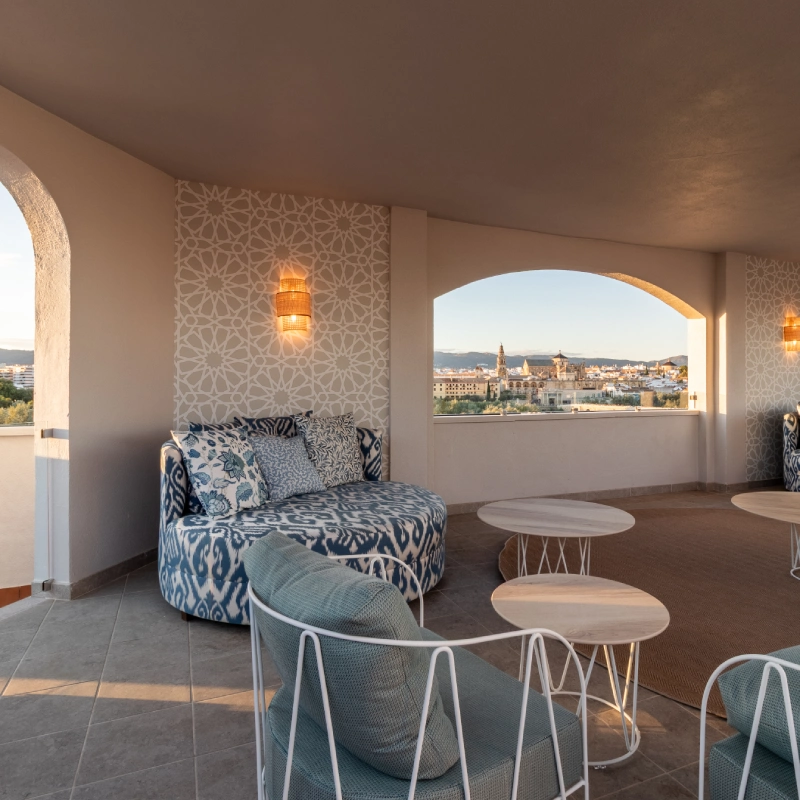 Terraza con sof&aacute;s elegantes y vista urbana desde un arco en la pared.