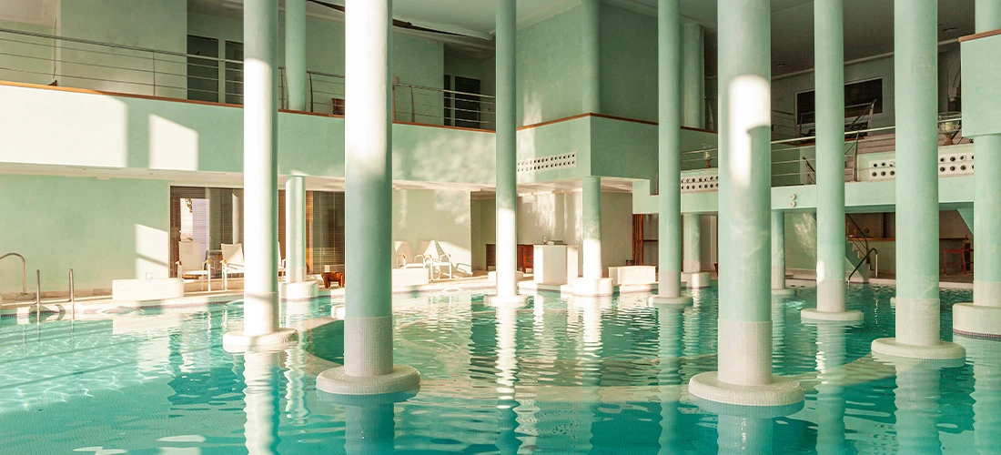 Piscina cubierta de spa con columnas de color verde menta y luz natural.