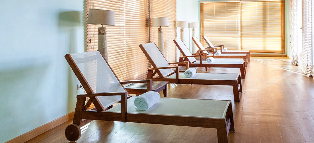 Sala de descanso con tumbonas de madera, toallas y persianas de listones.