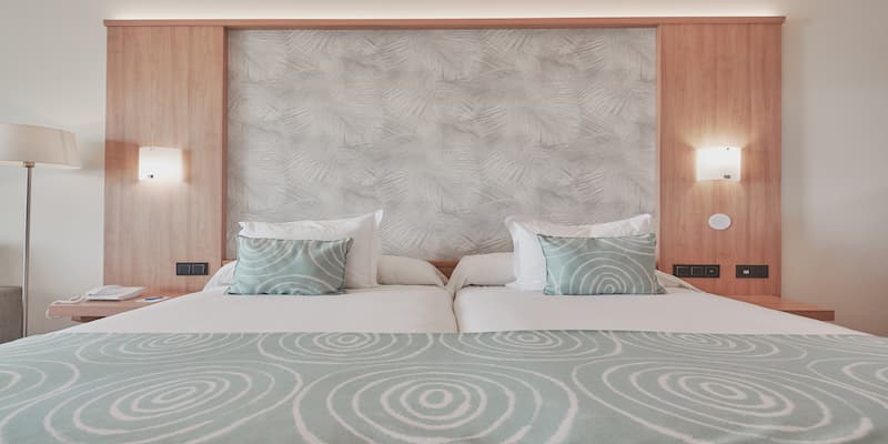 Cama doble en habitaci&oacute;n de hotel con cabecero de patr&oacute;n geom&eacute;trico y luces de pared.