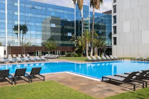 A serene view of a luxury hotel pool surrounded by lounge chairs and palm trees.