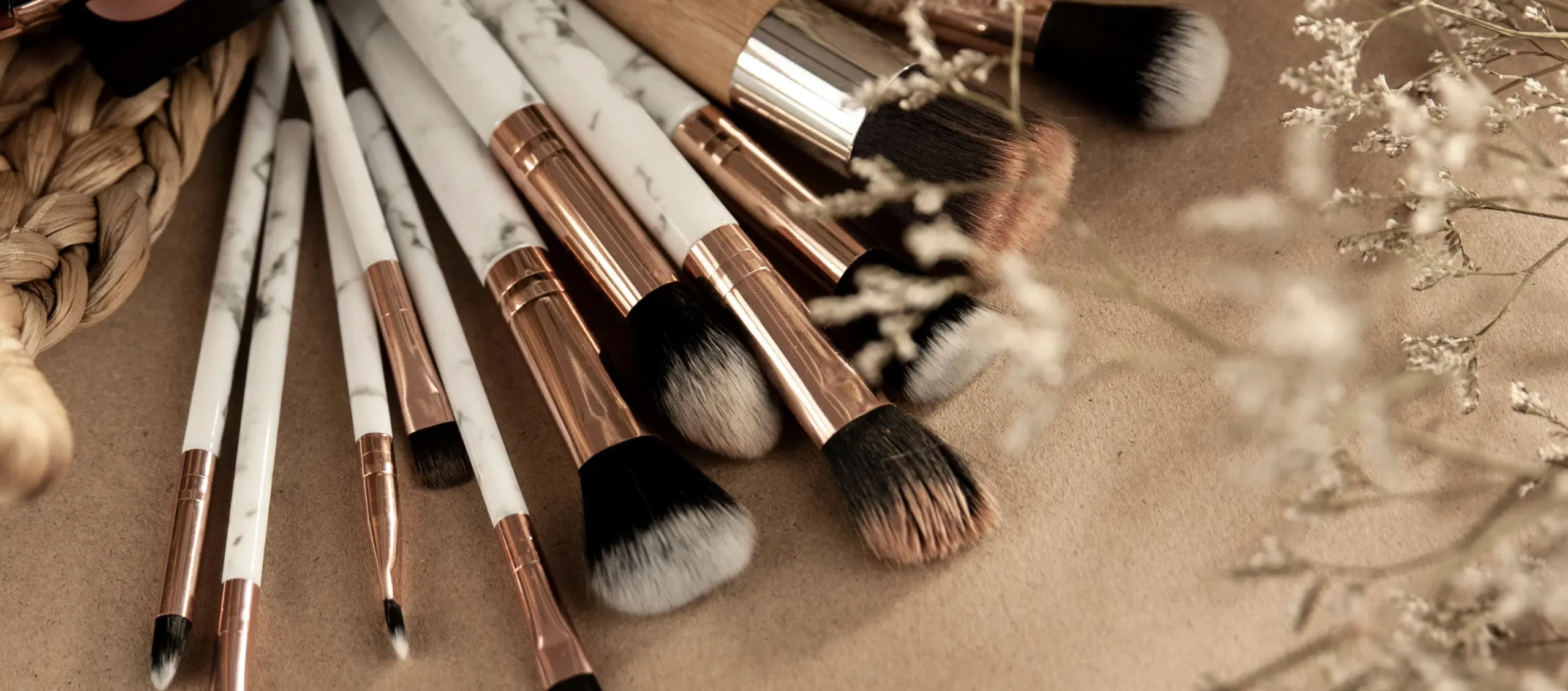 A collection of marble and rose gold makeup brushes on a textured surface