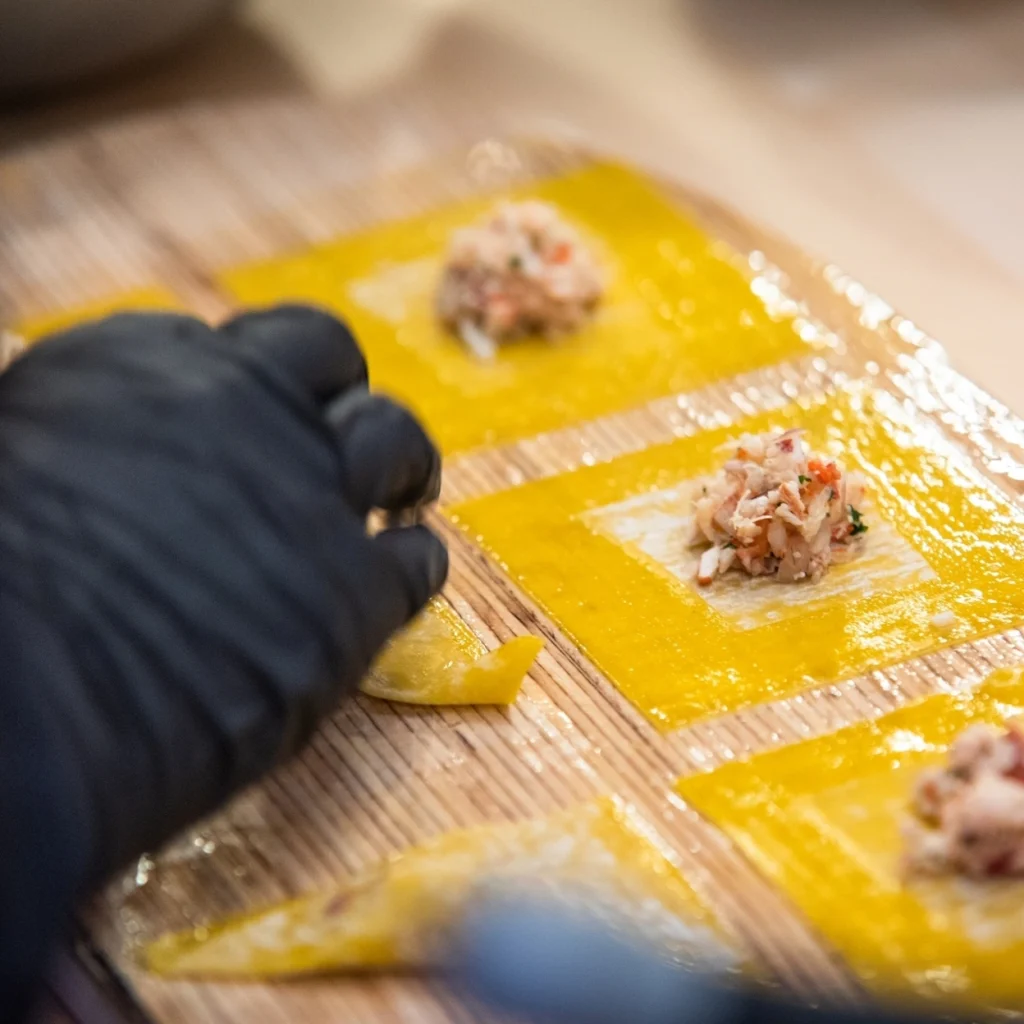Close-up of a hand assembling handmade dumplings with yellow dough and crab filling