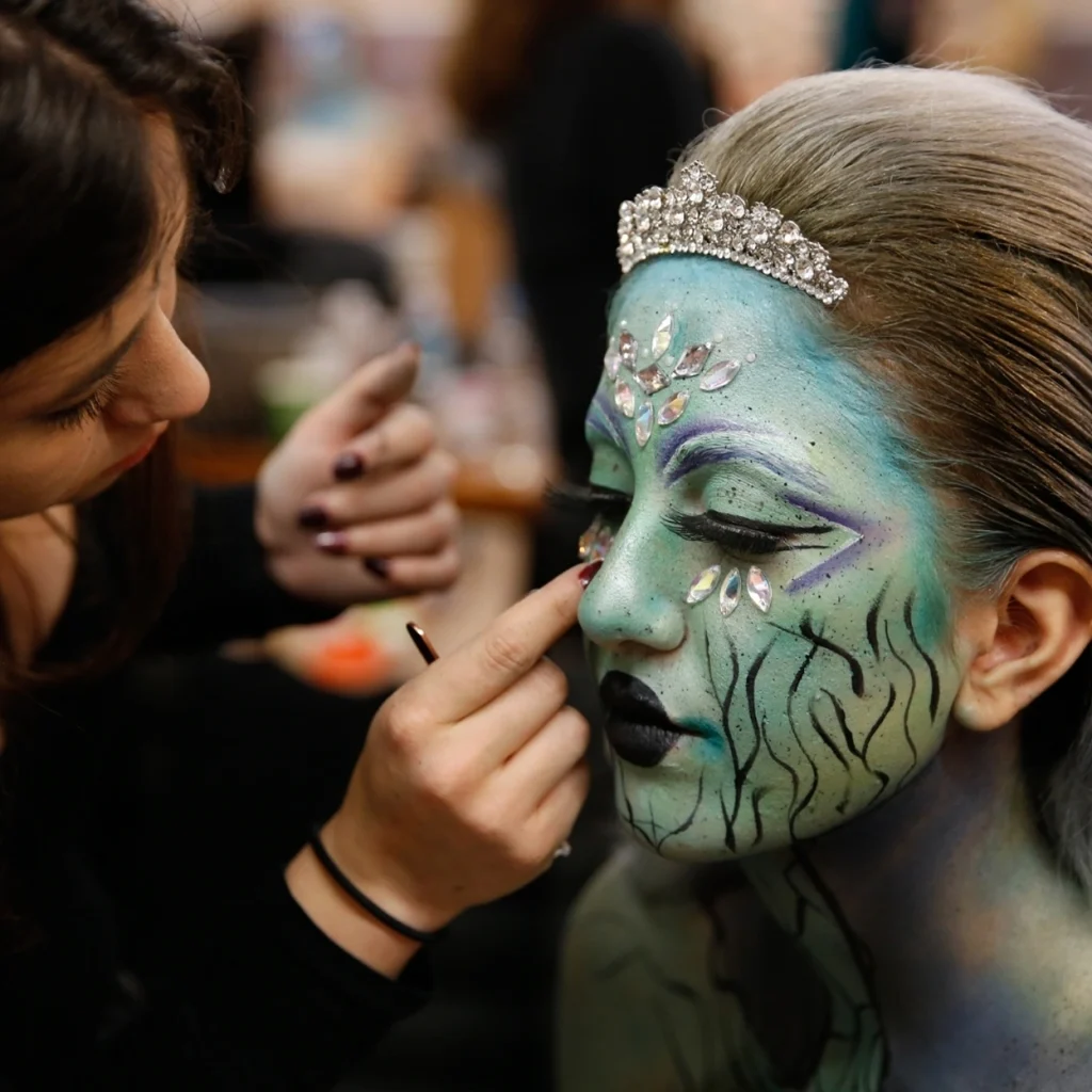 Woman receiving artistic makeup with shiny details on her face.