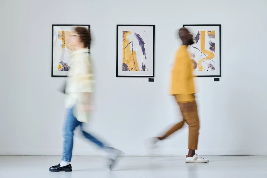 Two visitors walking through an art gallery with abstract paintings on the wall