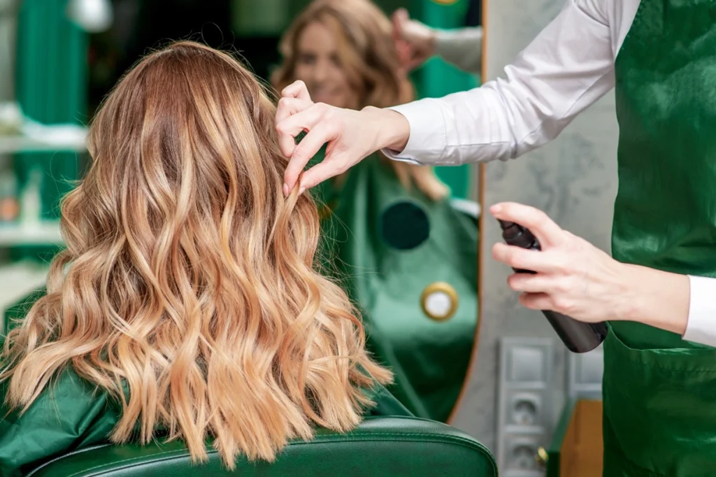 A hairstylist applying a hair product to a client's wavy hair in a salon