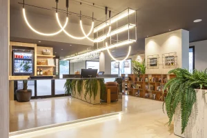 Hotel reception with warm lighting, sleek desk, hanging greenery, curved pendant lights, wooden shelves, and large plants