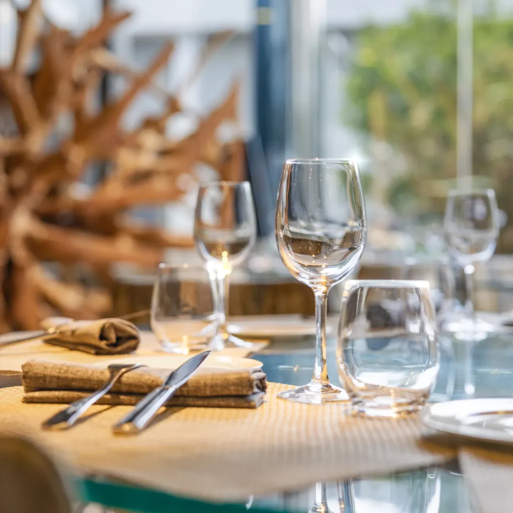 An elegant table setting with wine glasses and silverware sits before a blurred background of natural wood and greenery