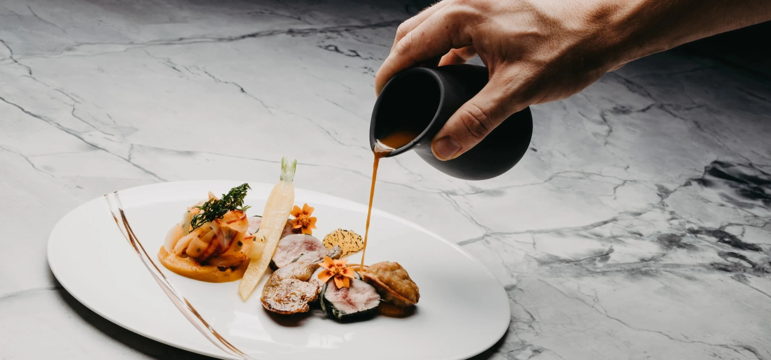 A chef pouring sauce over an elegantly plated gourmet dish