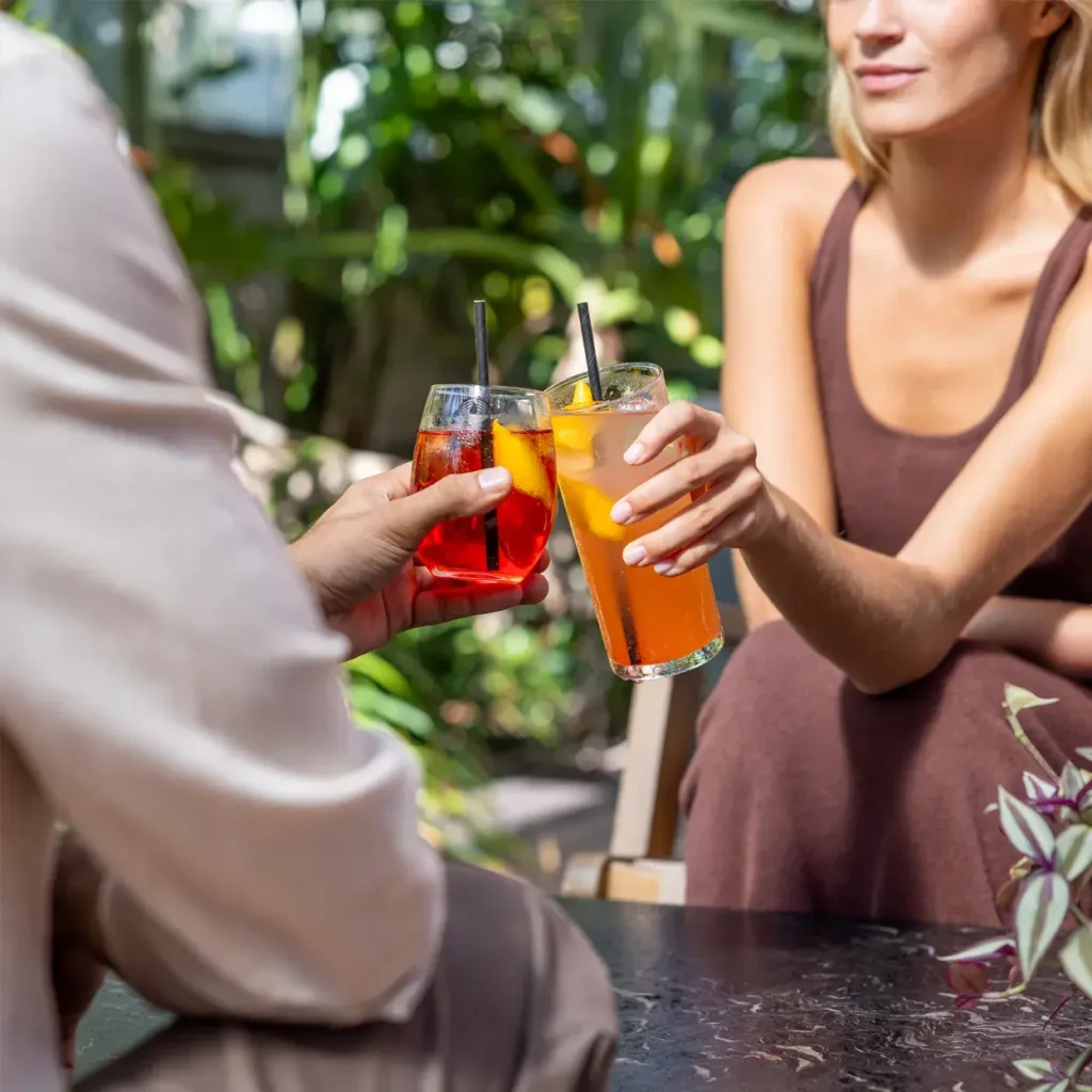 Two friends toasting with colorful cocktails in a lush garden setting.