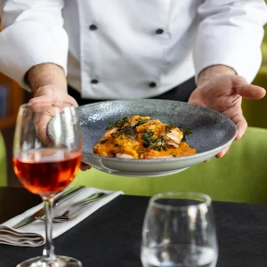 A chef presents a plate of food garnished with herbs