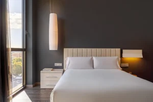 A modern room with a bed, nightstand, and large window