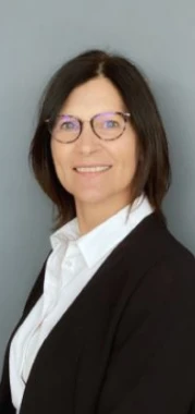 Une femme souriante portant des lunettes, cheveux bruns, fond gris.