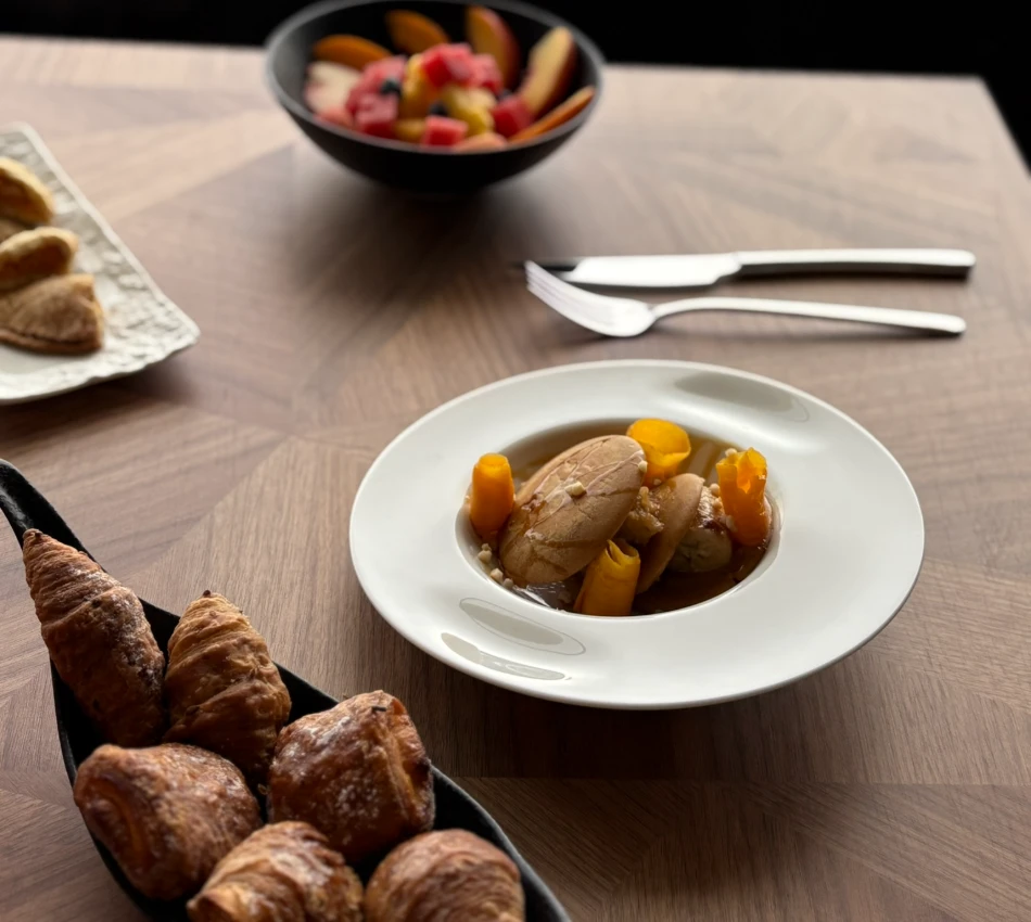 Mesa con croissants, plato de fondo y ensalada de frutas.