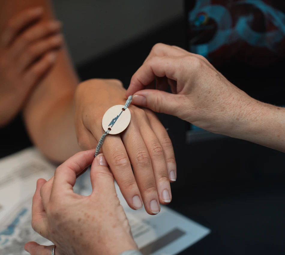Manos ajustando una pulsera con colgante en una mu&ntilde;eca.