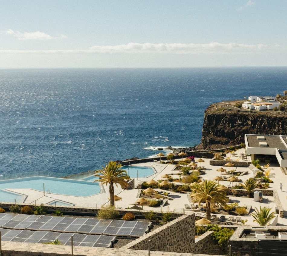 Complejo frente al mar con piscina y palmeras sobre un acantilado.