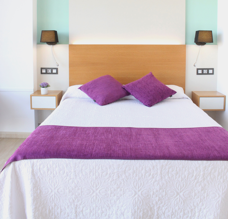 foto de habitacion doble con cabecero de madera con sabanas blancas y pleid y cojines de color