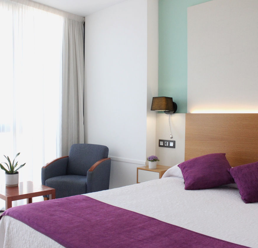 foto de habitacion doble con cabecero de madera con sabanas blancas y pleid y cojines de color