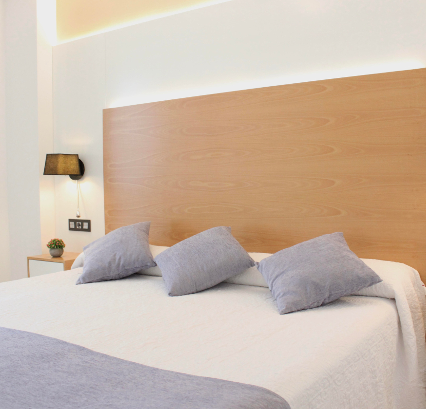 foto de habitacion doble con cabecero de madera con sabanas blancas y pleid y cojines de color