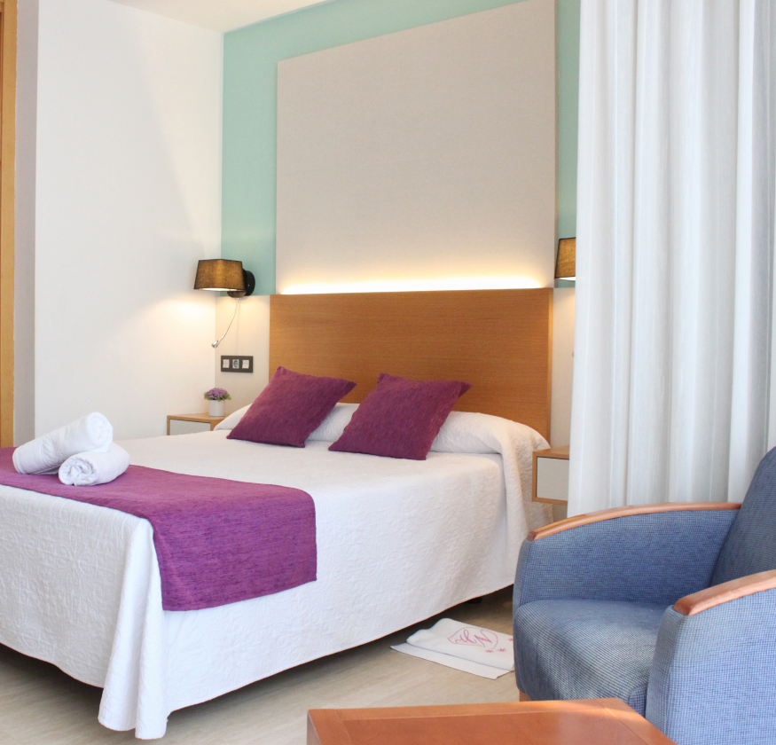 foto de habitacion doble con cabecero de madera con sabanas blancas y pleid y cojines de color