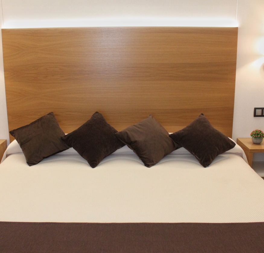 foto de habitacion doble con cabecero de madera con sabanas blancas y pleid y cojines de color