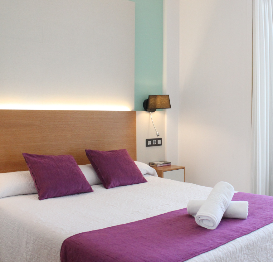 foto de habitacion doble con cabecero de madera con sabanas blancas y pleid y cojines de color