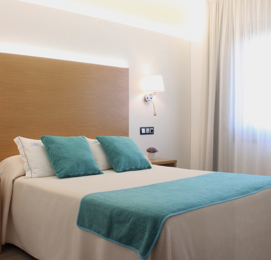 foto de habitacion doble con cabecero de madera con sabanas blancas y pleid y cojines de color