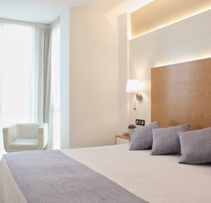 foto de habitacion doble con cabecero de madera con sabanas blancas y pleid y cojines de color