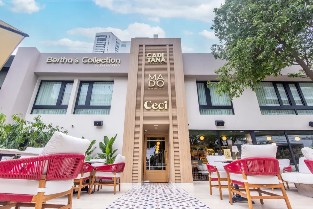 Fachada de hotel con terraza, sillas rojas y letrero &ldquo;Cada Tana&rdquo;