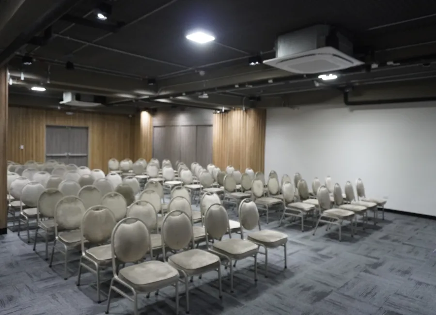 Sal&oacute;n de conferencias con sillas apiladas y proyector en techo industrial