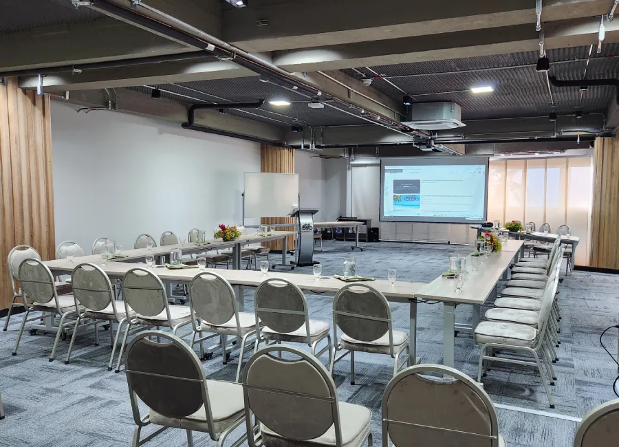 Sala de reuniones moderna con mesas, sillas y proyector en pared.