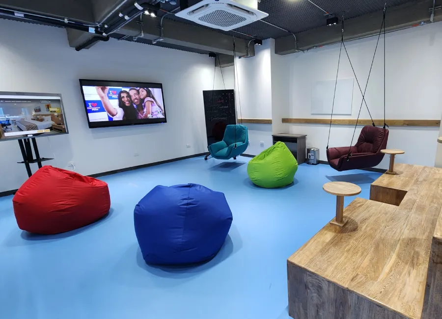Sala de ocio con sillones y puffs de colores, TV y mesa de madera.